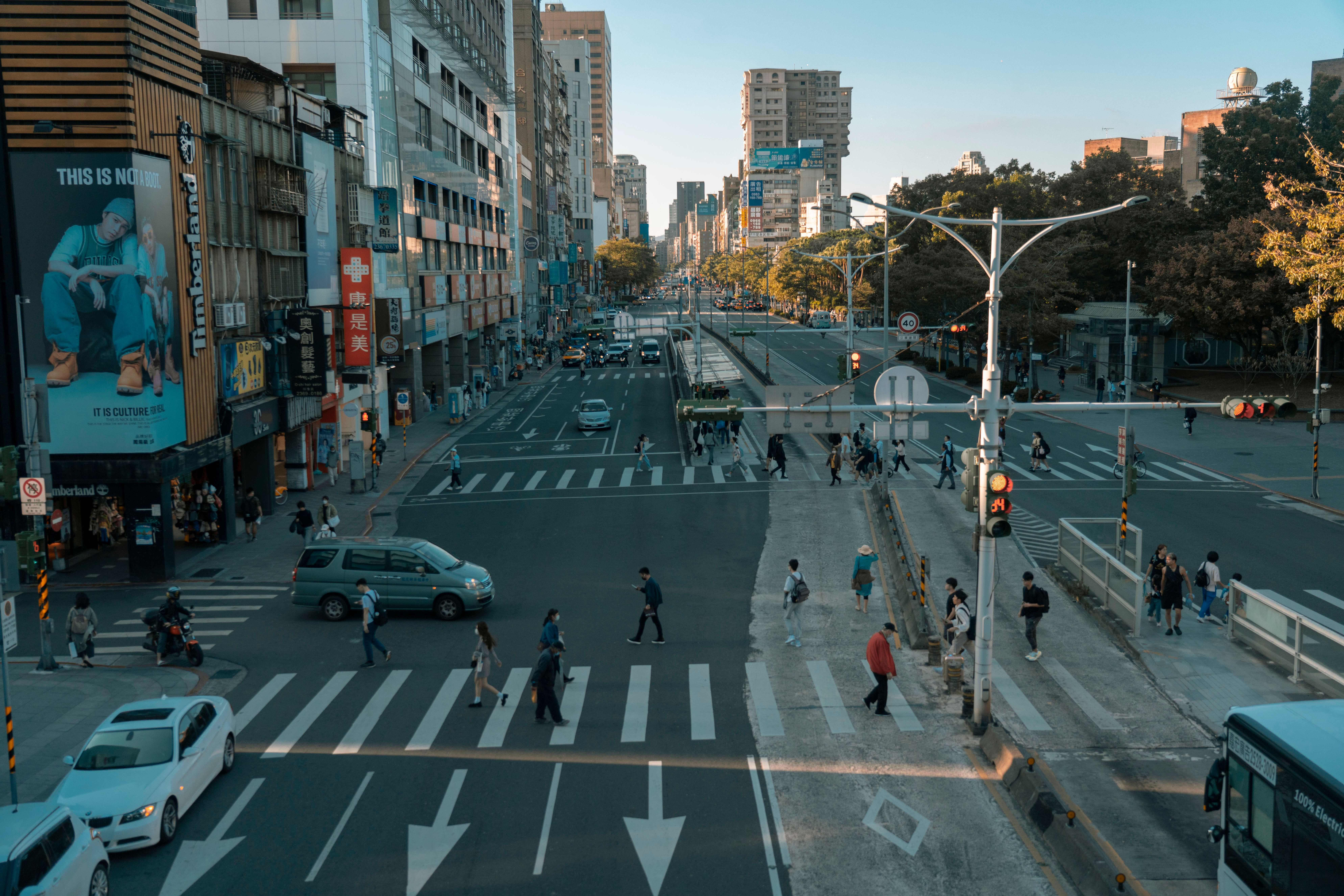 An aerial view of a busy city crosswalk with pedestrians and traffic under a clear sky.