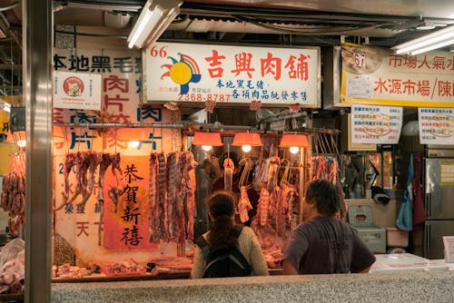 People Standing in front of a Butchers Market Stall in City 