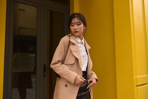 Free Young Asian woman in chic fashion standing against a vibrant yellow building facade. Stock Photo