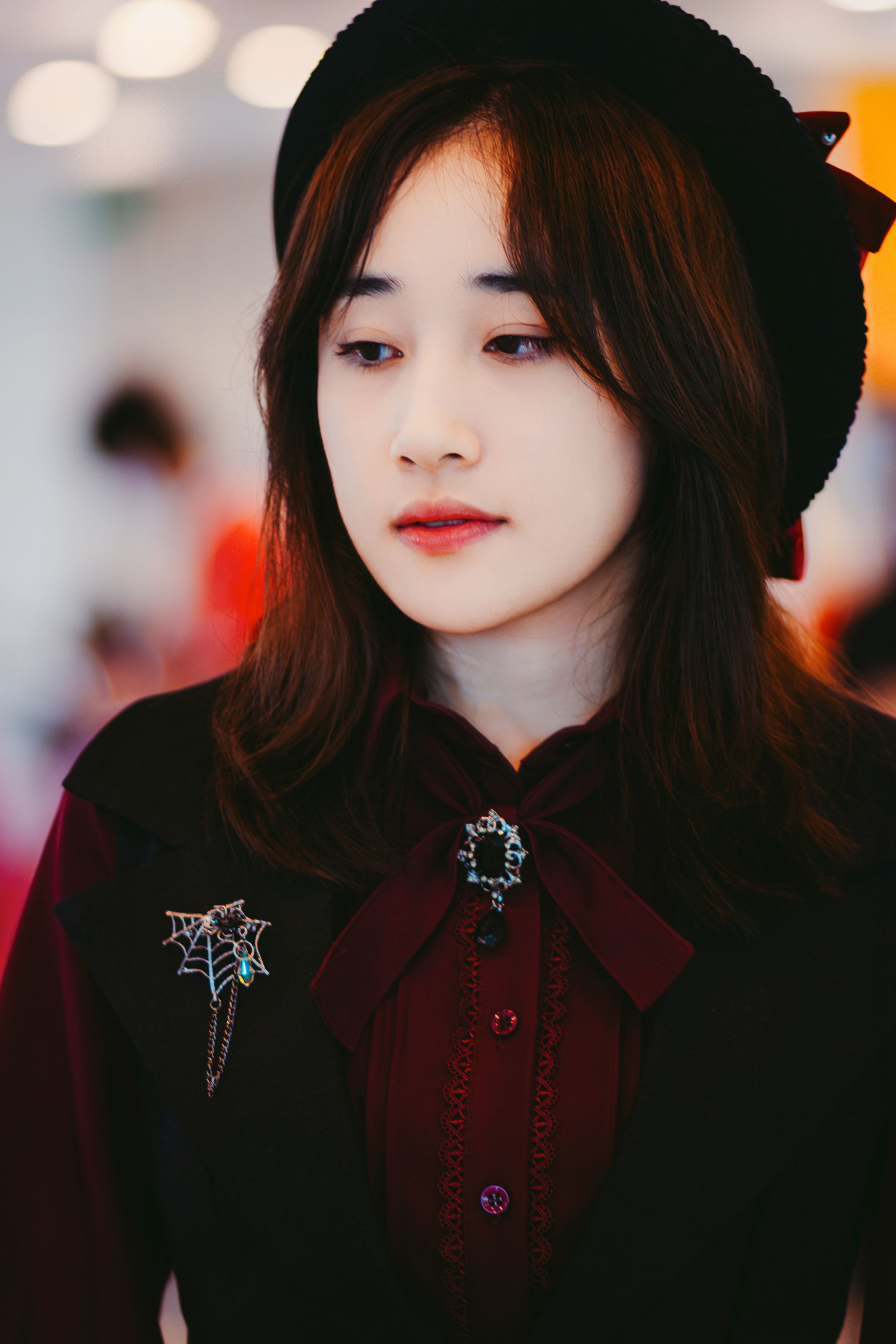 Young woman in gothic attire with black hat and brooch, looking pensive.