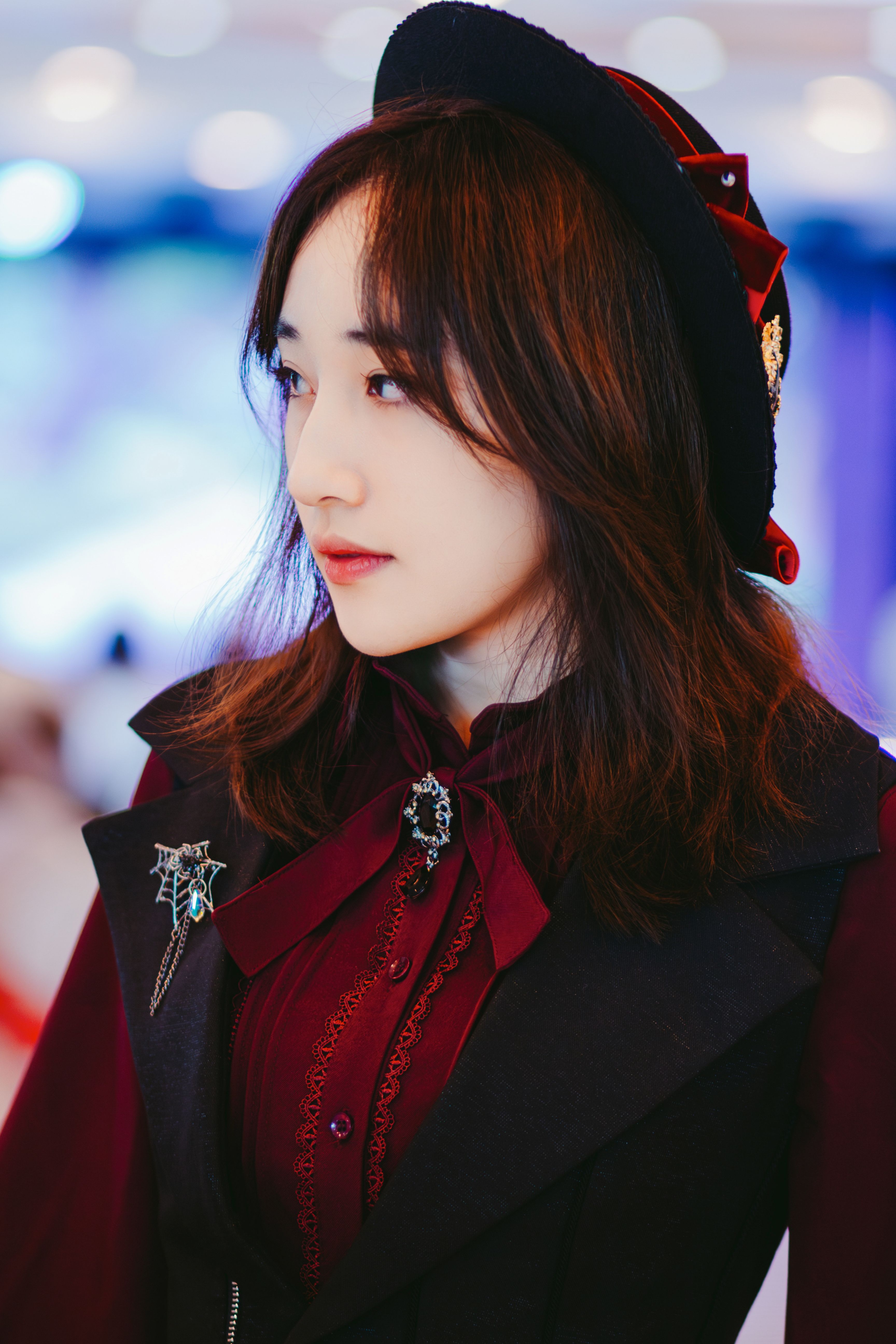 Portrait of an Asian woman in a stylish cosplay outfit with a brooch and black hat.