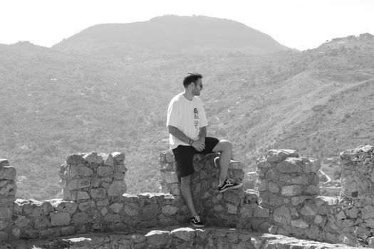 Black and white image of a man sitting on an ancient ruin wall in Cefalù, Italy.