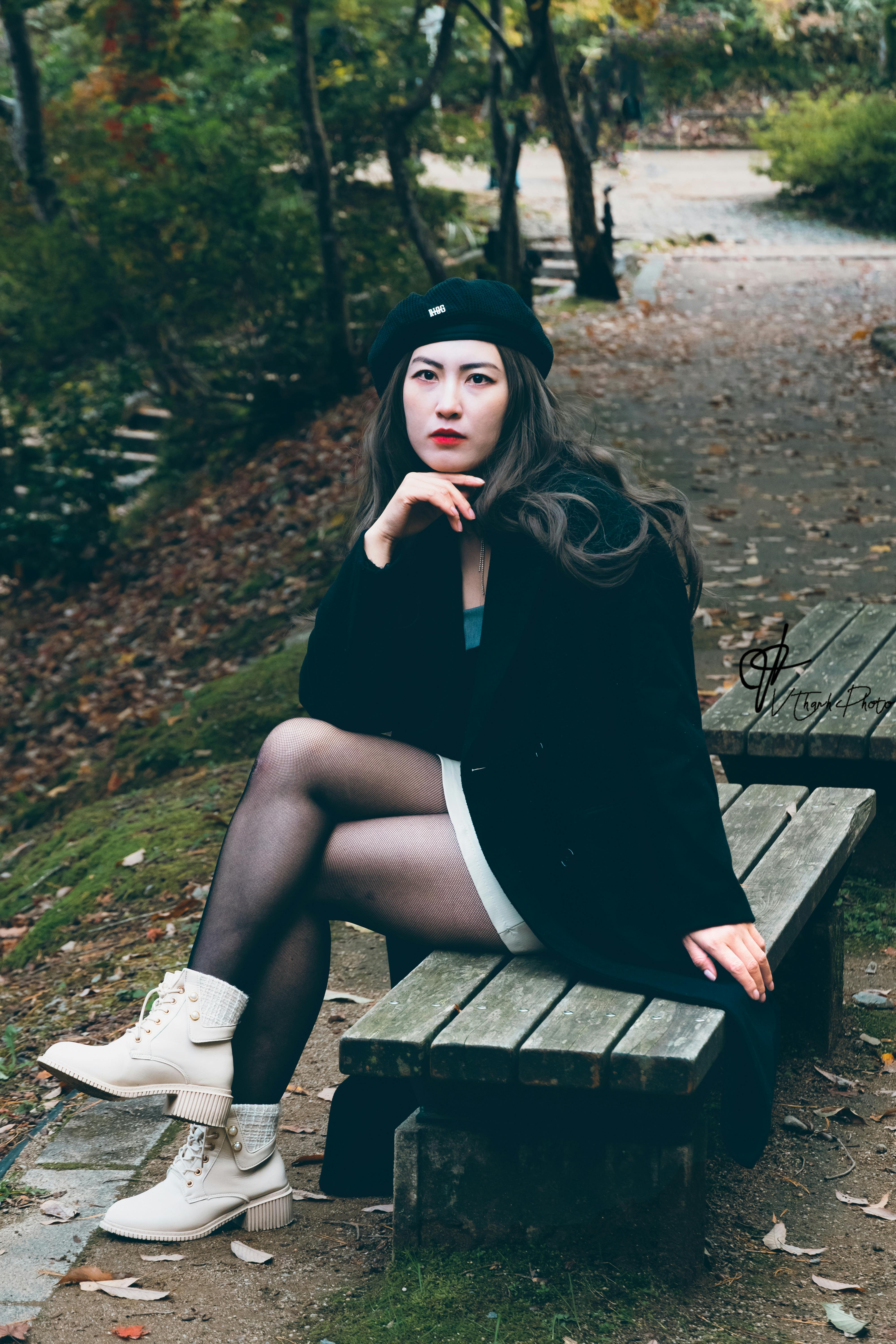 Woman in autumn attire posing thoughtfully on a park bench.