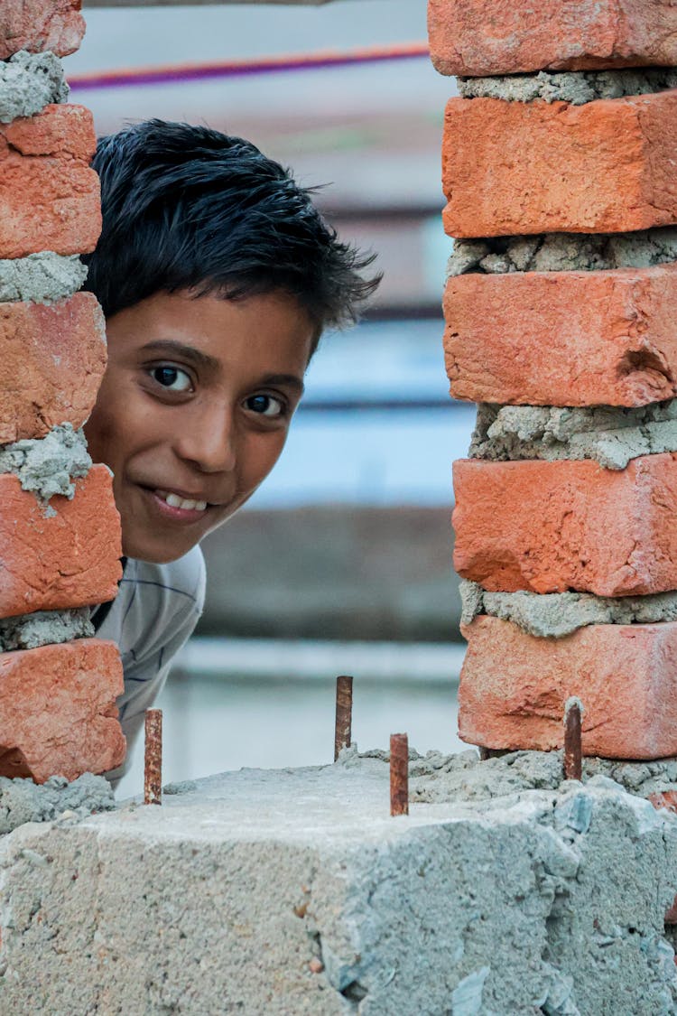 Smiling Child Looking Through A Hole In The Wall Of A Building Under Construction