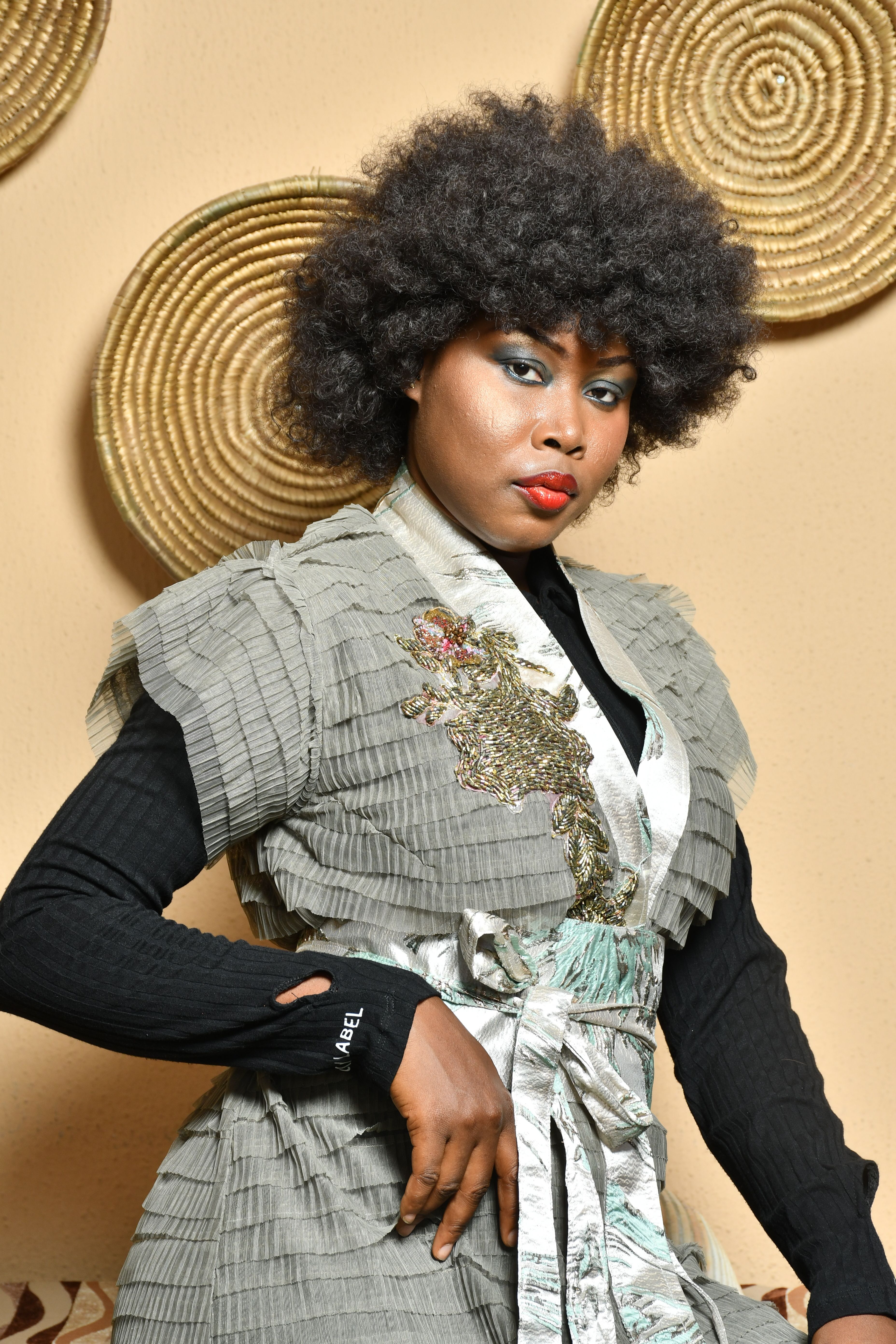 Stylish woman with curly hair posing in fashionable attire against decorated wall.