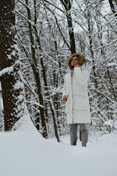Model in a White Padded Winter Coat with a Fur-Trimmed Hood Standing in a Snow Covered Forest