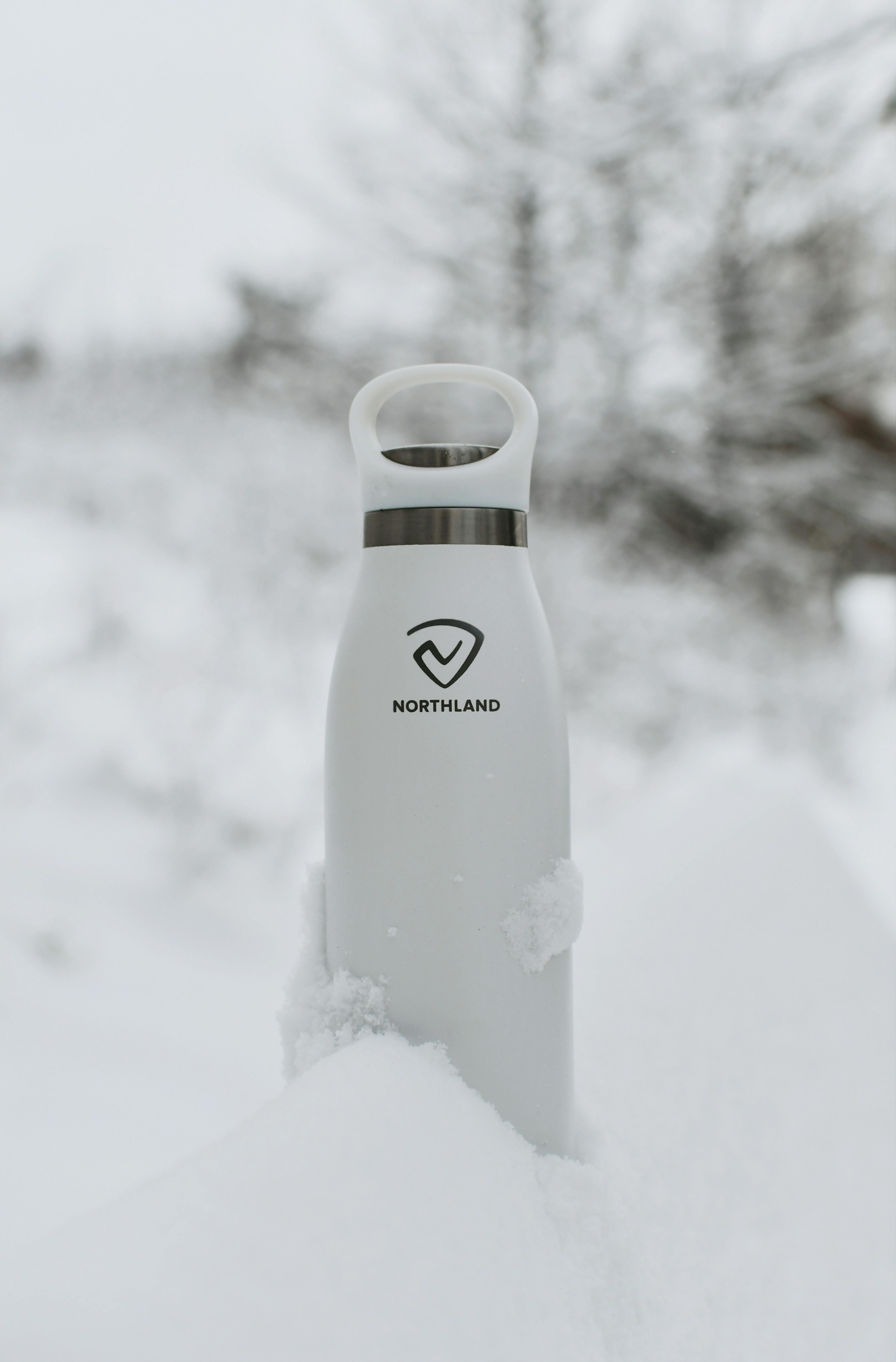 Stylish white vacuum flask by Northland in a snowy winter setting, offering insulation for drinks.