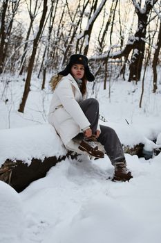 A young woman in a white jacket and ushanka poses on a snowy log in a winter forest.