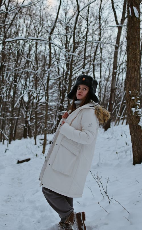 Free Woman wearing a white coat and cap in a snowy forest, enjoying a winter walk. Stock Photo