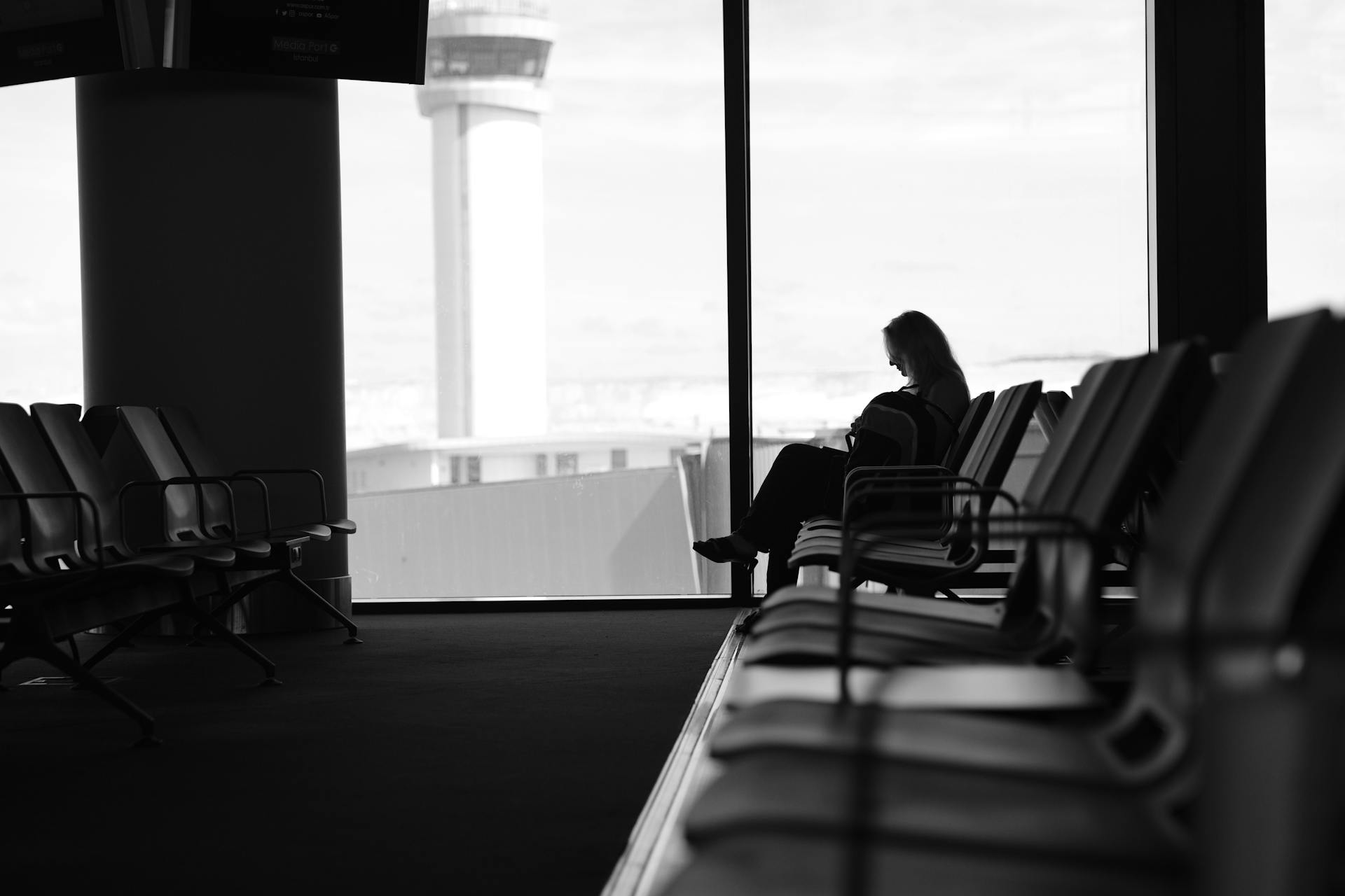 Silhouette of a woman sitting in an airport terminal lounge, with view of control tower.