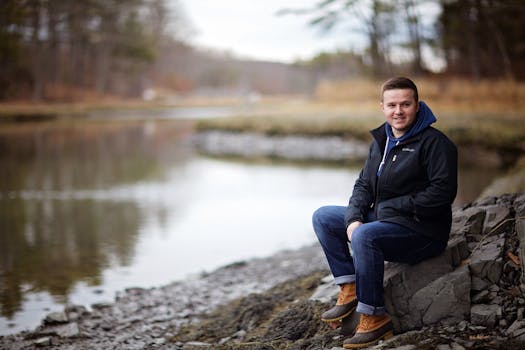 一个男人面带微笑，坐在宁静的湖边，四周被大自然环绕