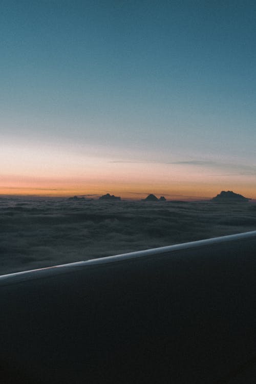 Mountains Peeking Out From the Cloud Cover Seen Above the Plane Wing at Sunset