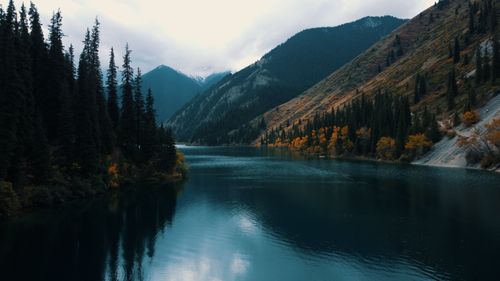 Free Tranquil lake surrounded by autumn foliage and mountains on a cloudy day. Stock Photo