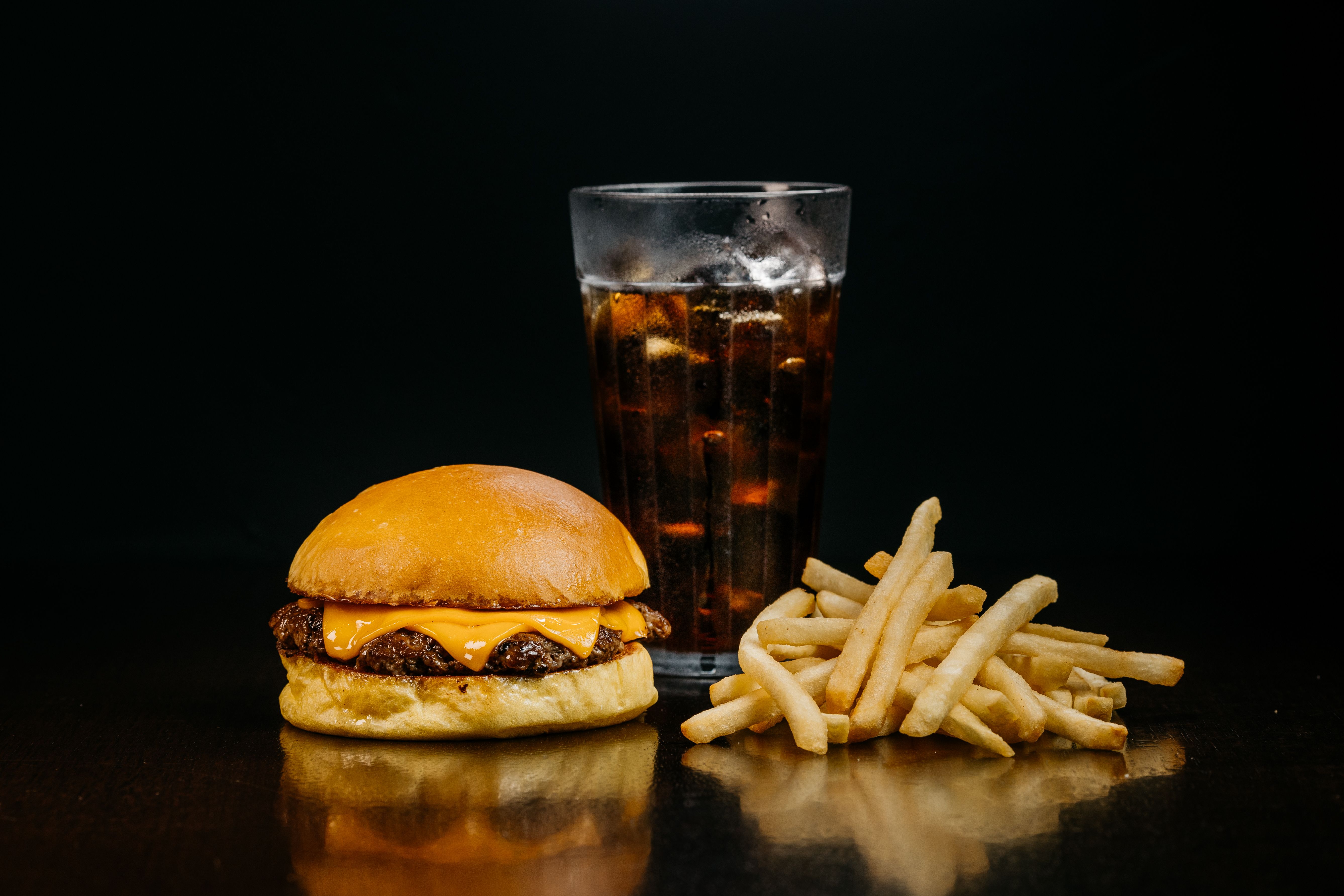 Delicious cheeseburger with fries and soda on a dark background.