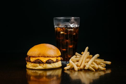 Delicious cheeseburger with fries and soda on a dark background.