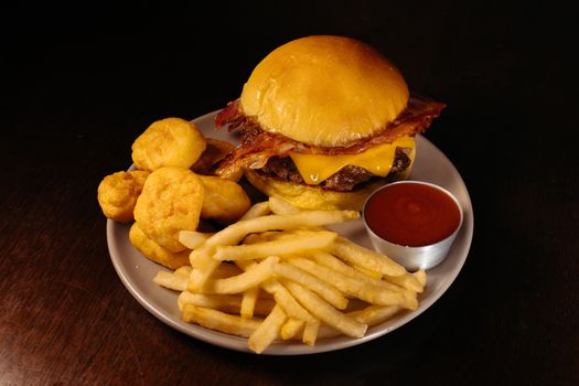 Tasty cheeseburger with bacon, fries, and nuggets on a plate with ketchup sauce.