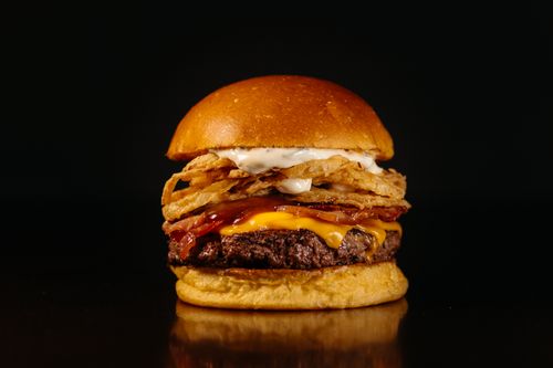 Free Close-up shot of a gourmet cheeseburger with crispy toppings, against a dark backdrop. Stock Photo