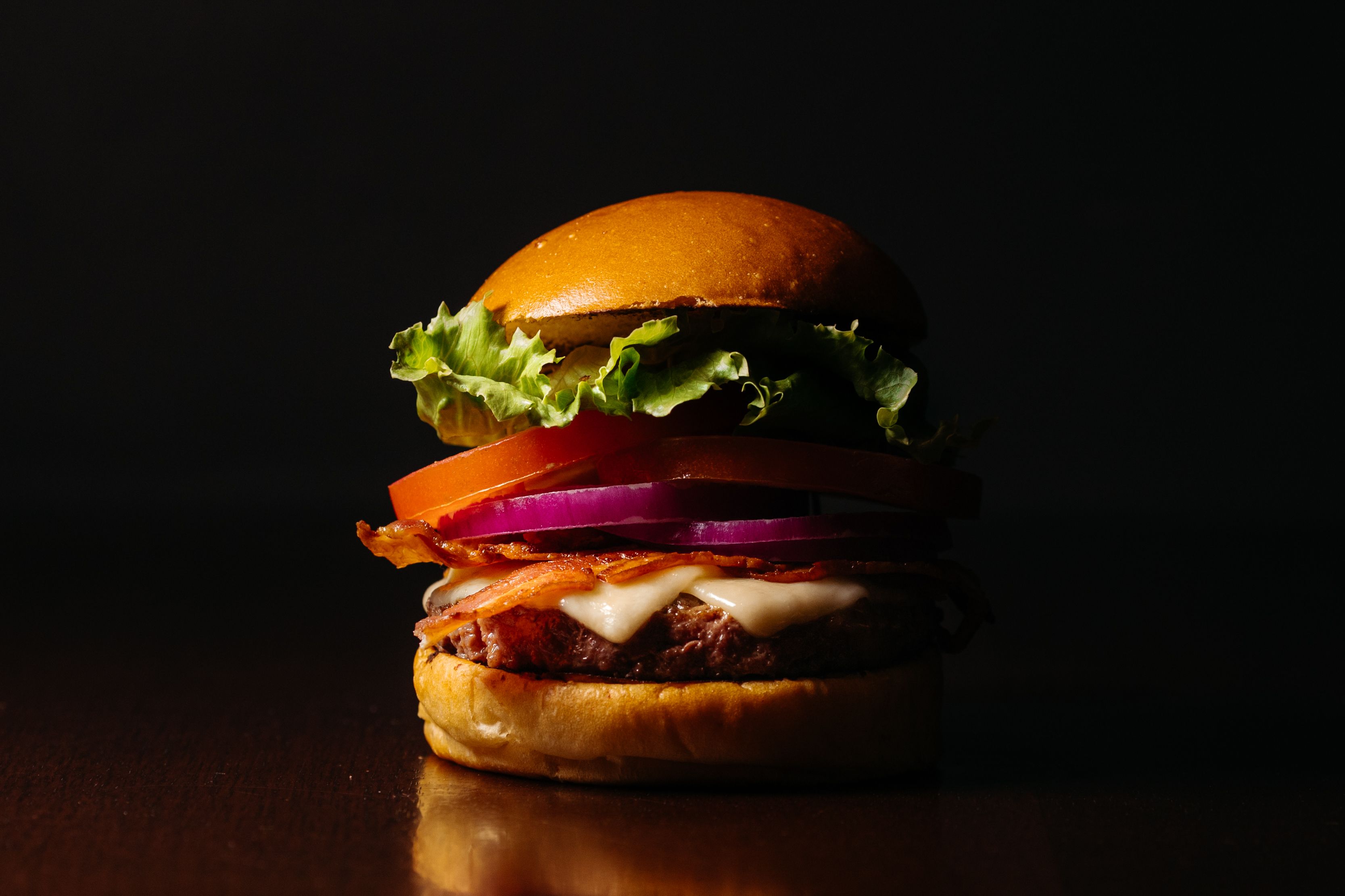 Mouth-watering gourmet burger with cheese, lettuce, tomato, and onion, perfectly stacked and lit.