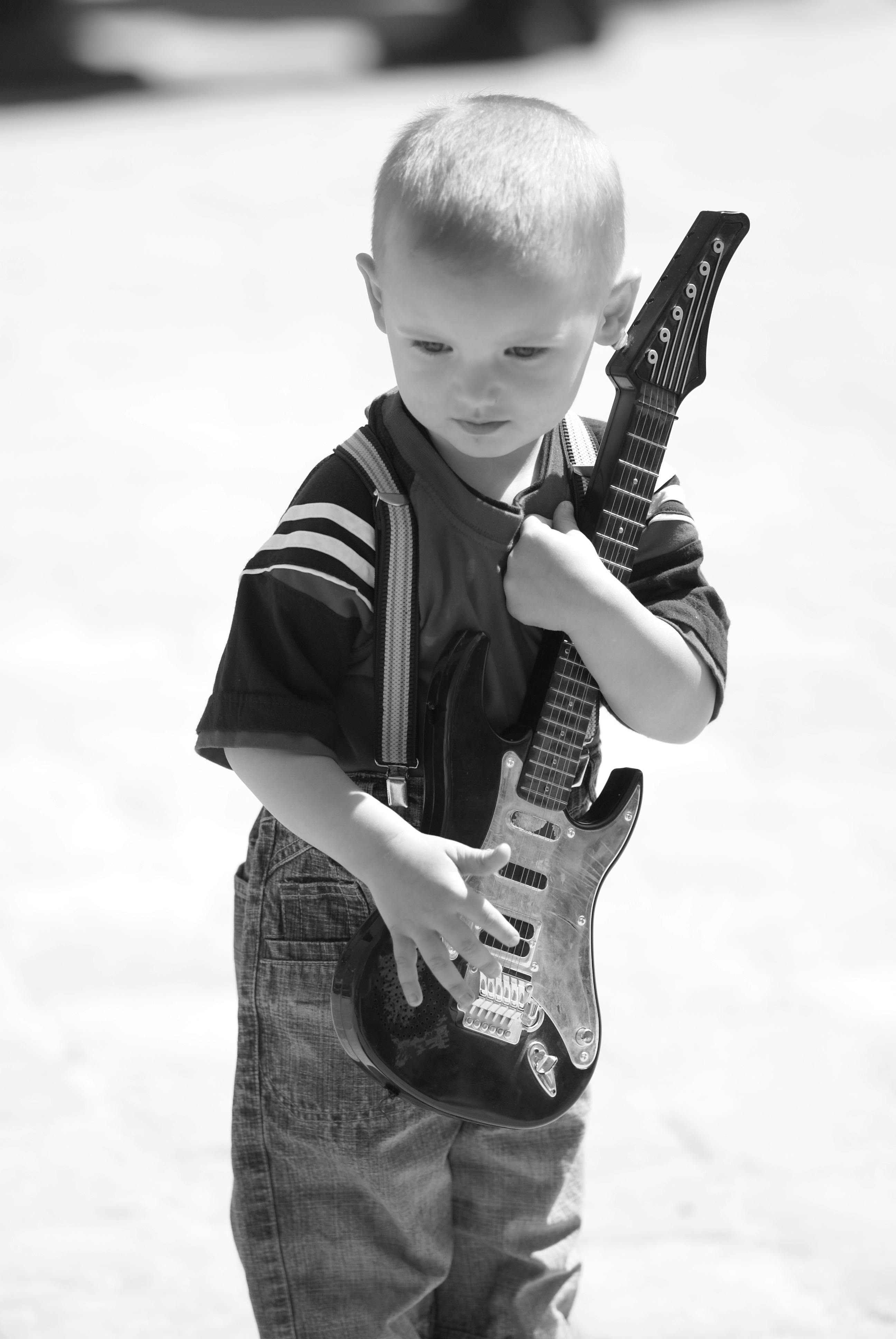 Charming black and white photo of a child holding a toy guitar outdoors, showcasing innocence and curiosity.
