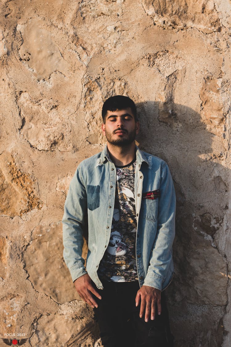 Man In Jean Jacket Standing By Stone Wall