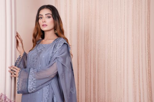 Free Stylish woman in embroidered blue dress posing indoors with serene expression. Stock Photo