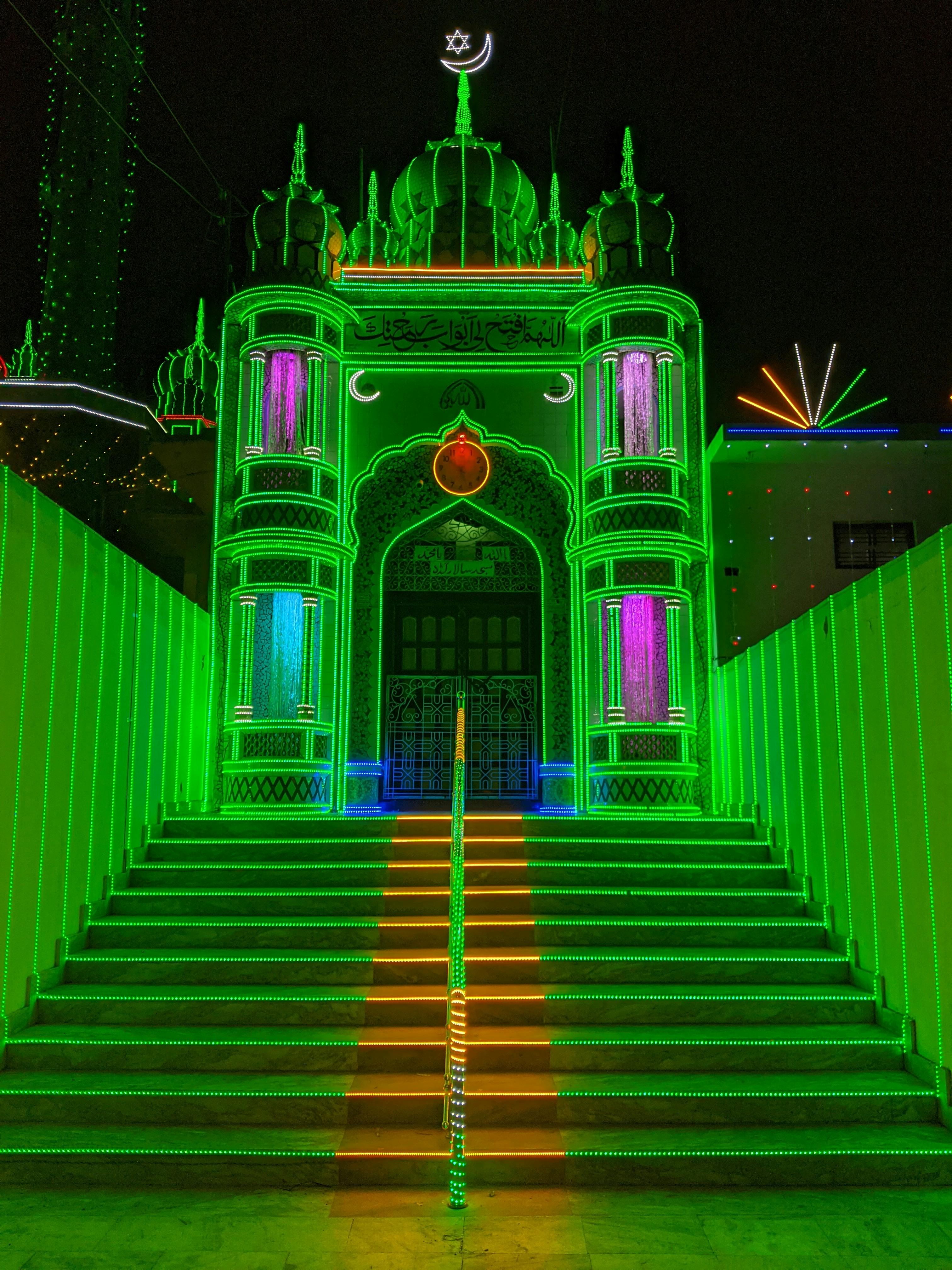 Vibrant nighttime shot of a mosque in Tanda, India, with colorful lights and decorative columns.