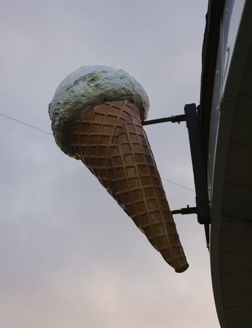 Free A large ice cream cone decoration attached to a building facade, seen outdoors against a cloudy sky. Stock Photo