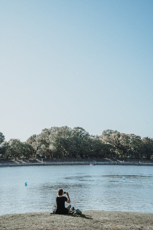 Woman Sitting and Photographing River 