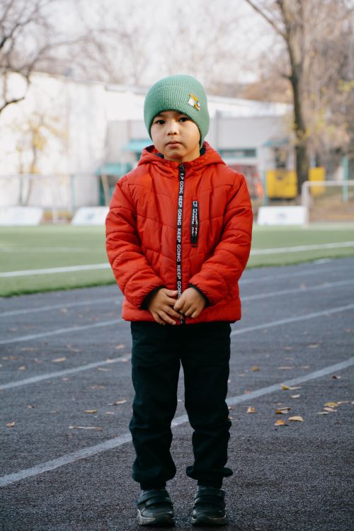 Free Portrait of a young boy in a red jacket and green hat standing on an urban street in Almaty, Kazakhstan. Stock Photo