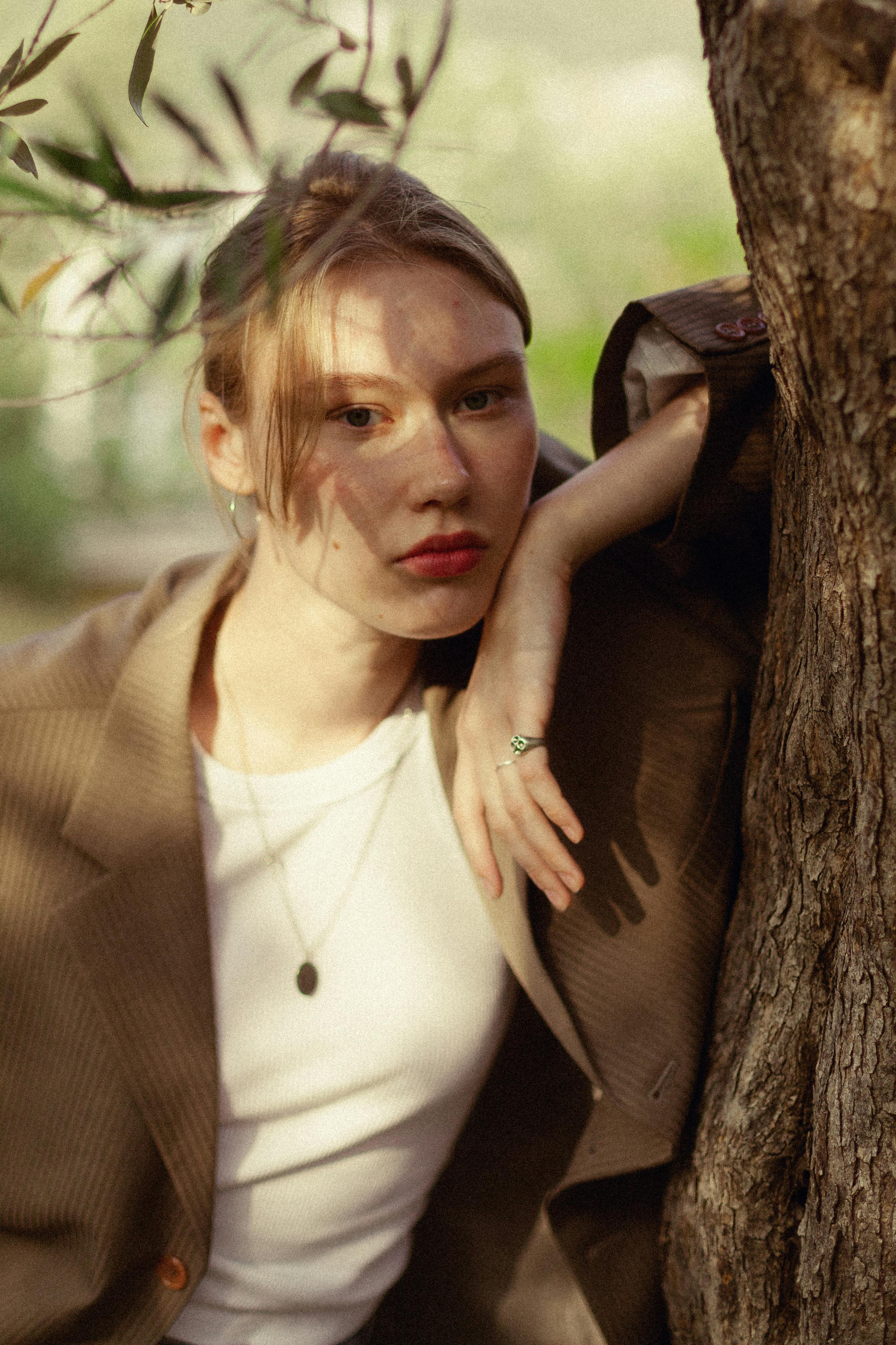 Sophisticated portrait of a woman in a blazer, leaning against a tree outdoors.