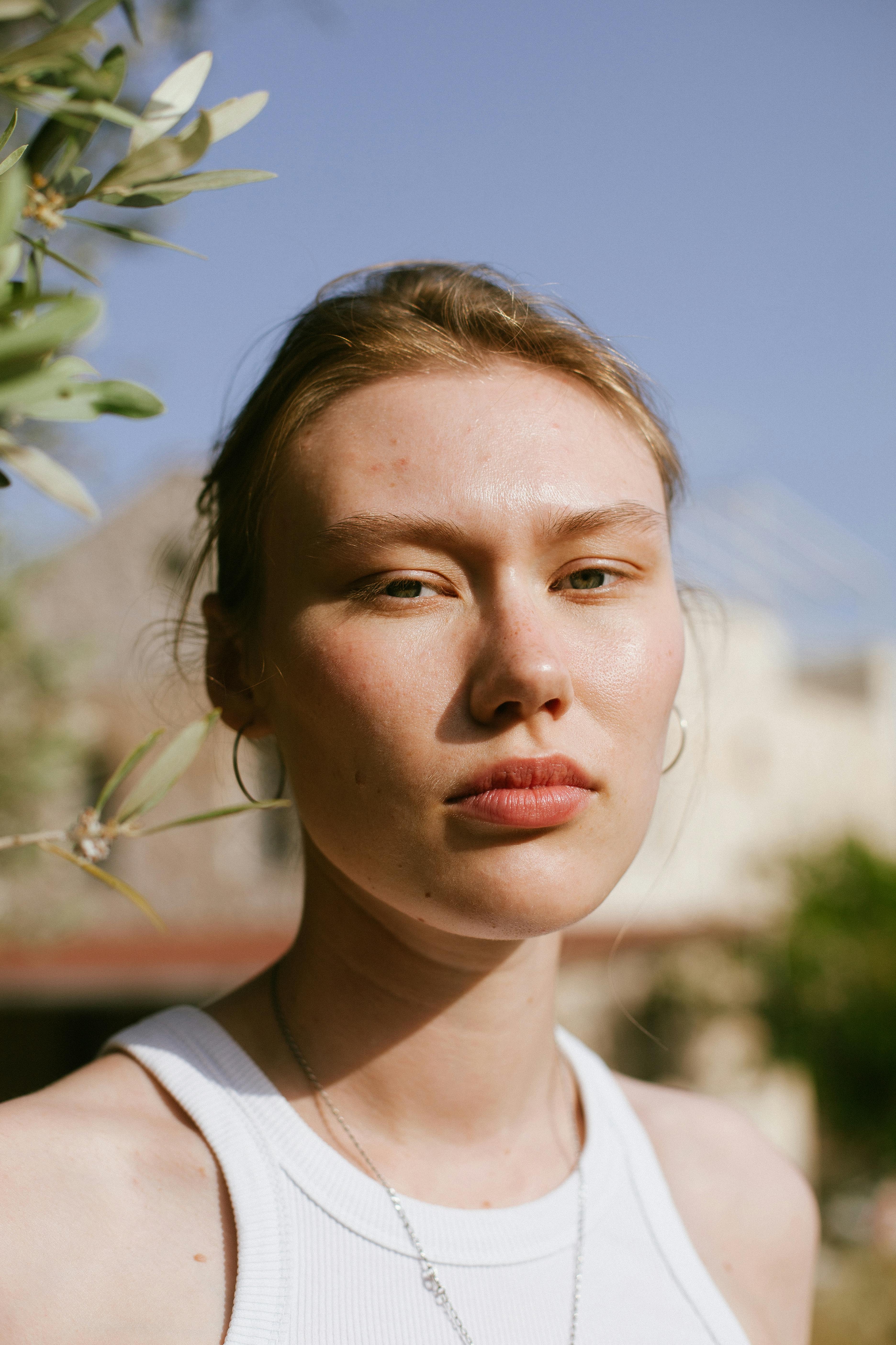 Close-up of a woman in natural sunlight, with a serene expression and outdoor setting.