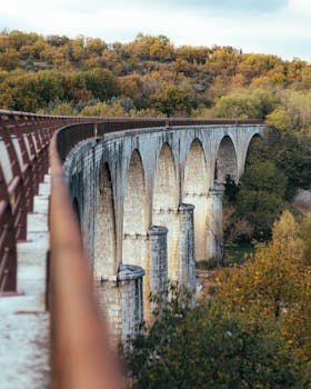 Explore the stunning arched stone bridge in Vogüé, France, surrounded by lush countryside.