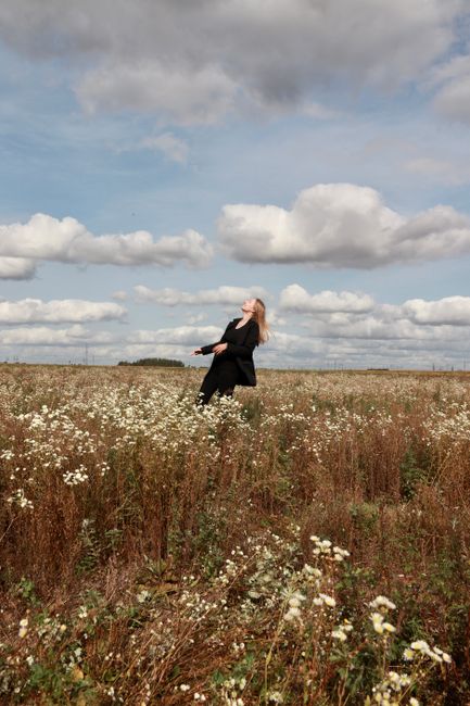 A woman embraces the warm sunlight in a blooming summer hayfield, surrounded by clouds.