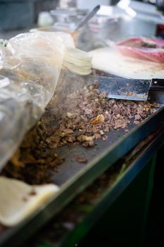 A close-up of a street vendor preparing fresh meat for tacos on a grill, capturing the vibrant food scene.