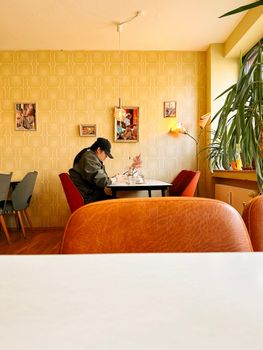A man sits alone in a retro-styled café in Cologne, Germany, using a smartphone.