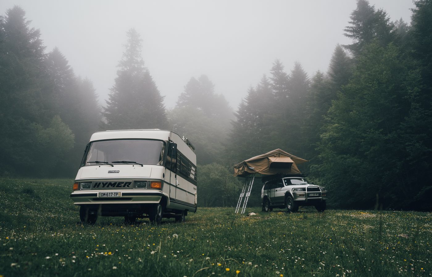 Scenic view of RV and tent in a foggy forest meadow, perfect for adventurous campers.