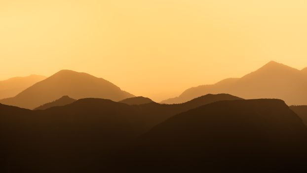 Sunset view of mountain silhouettes with warm orange hues in the sky.