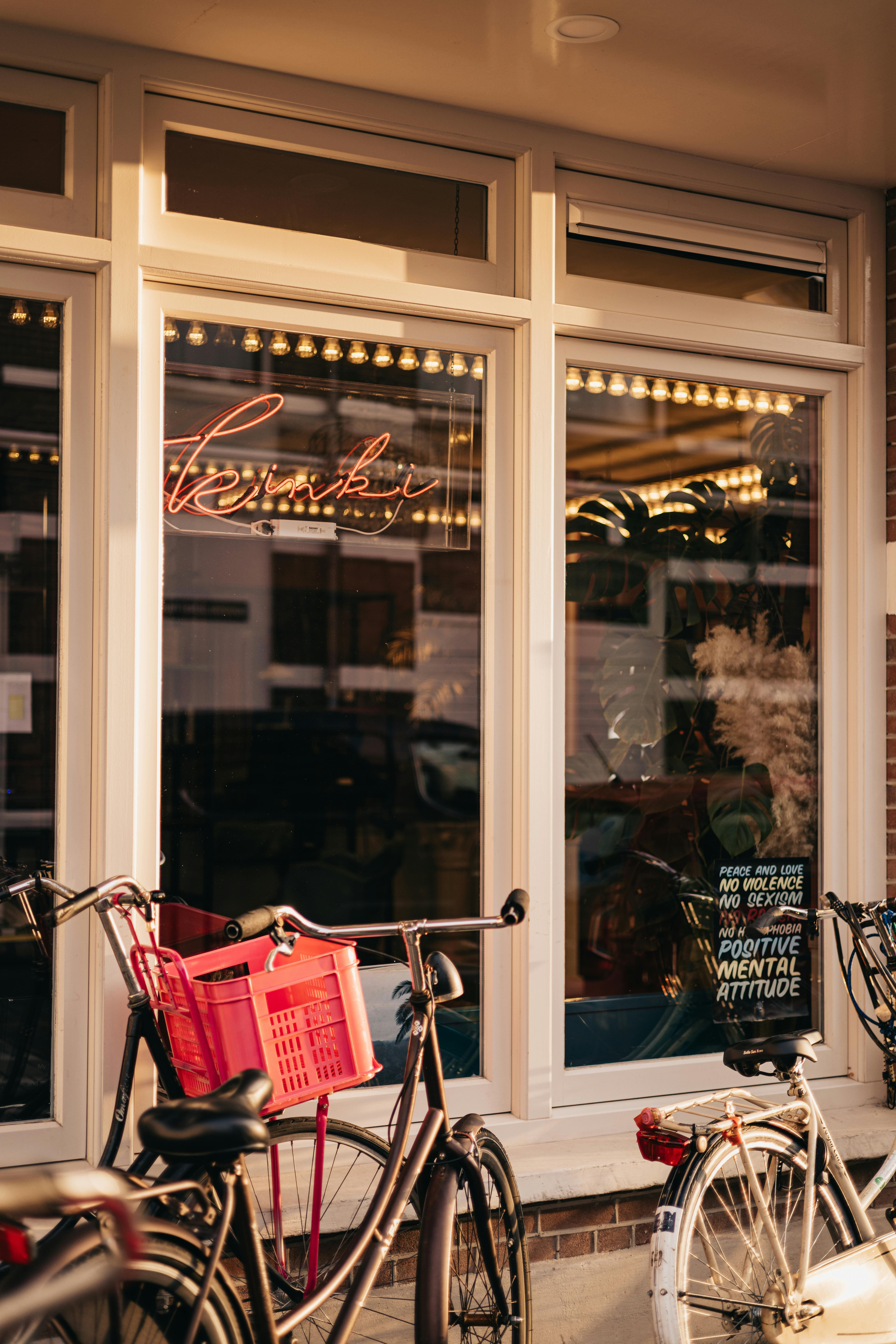 Outdoor shot of bicycles parked in front of a café window with a neon sign and motivational poster.