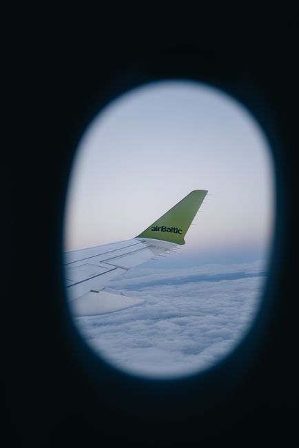 View of airplane wing at sunrise, capturing serene clouds from the window of an airBaltic flight.