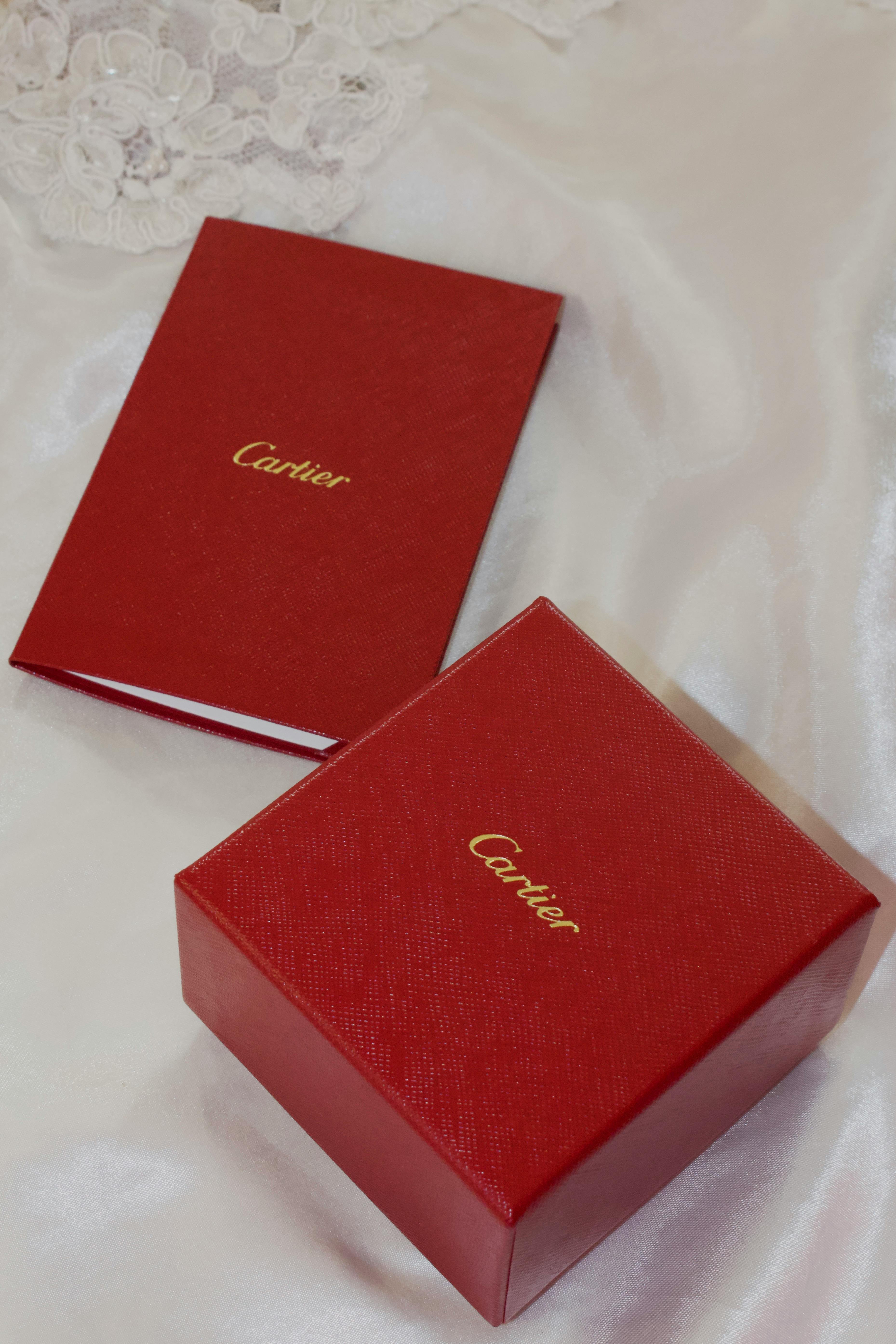 Red Cartier box and booklet on satin fabric, showcasing luxury and elegance.
