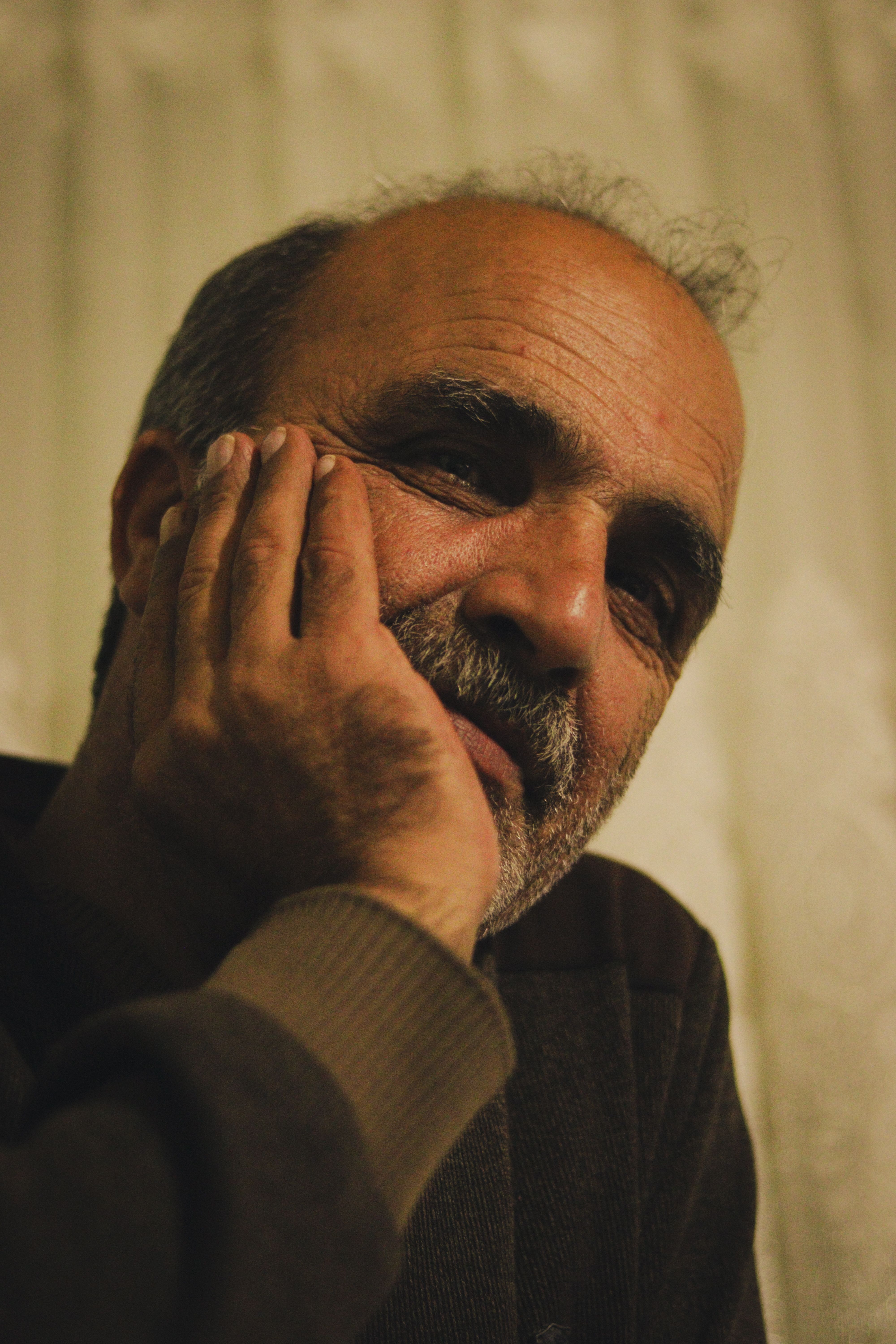 A serene portrait of an elderly man with a beard resting his head on his hand indoors.