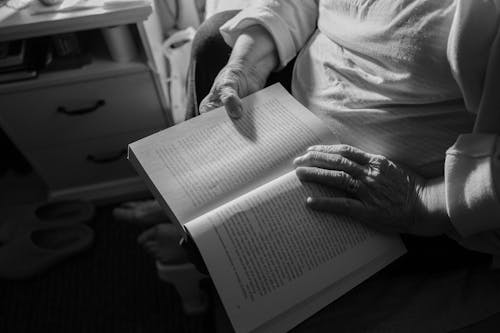 Free Elderly Person Hands Holding Book in Black and White Stock Photo