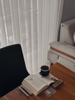 A peaceful study area with a book and coffee cup on a wooden desk by a window.