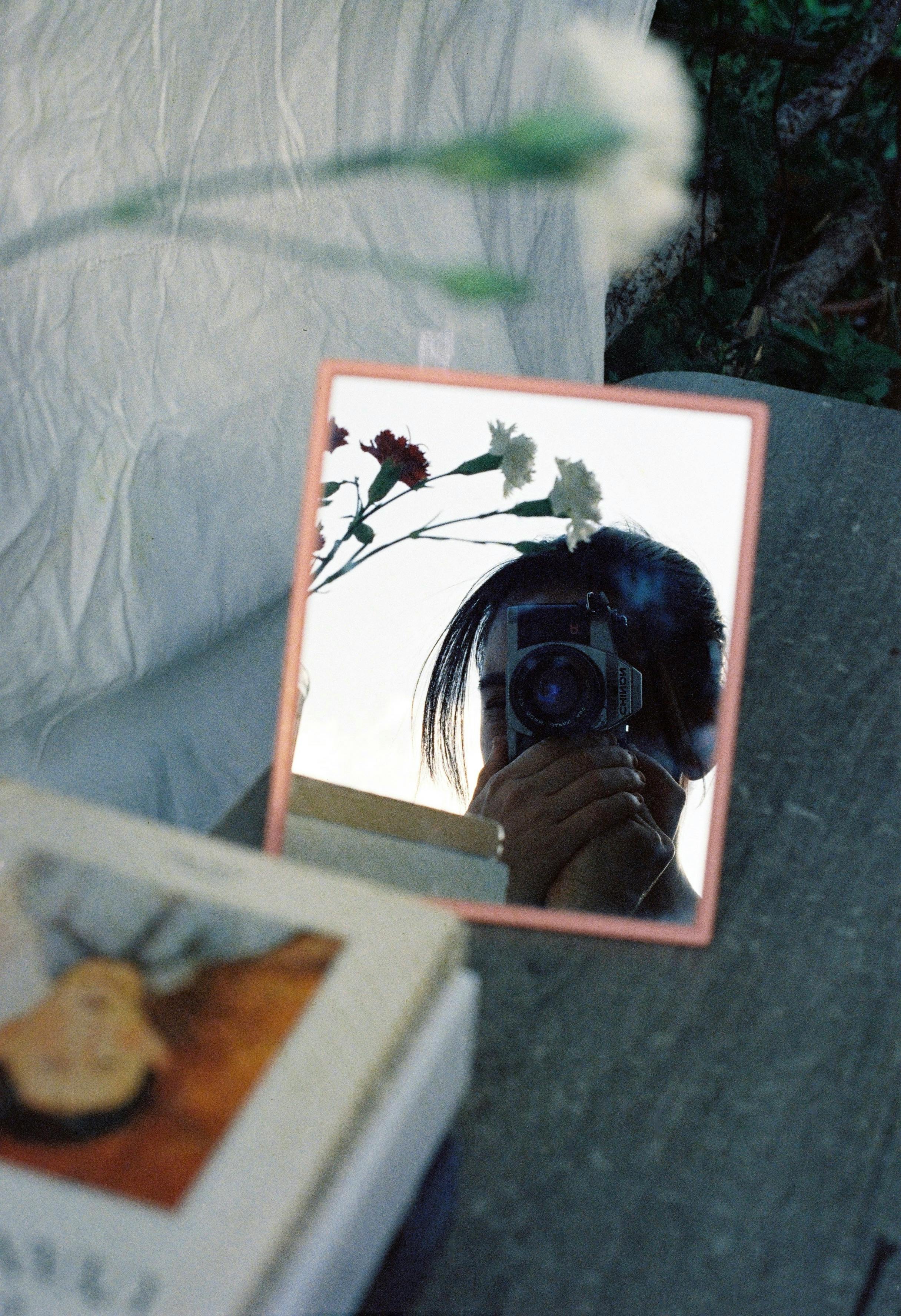 Creative reflection portrait with mirror, camera, and flowers showcasing artistic vibe.