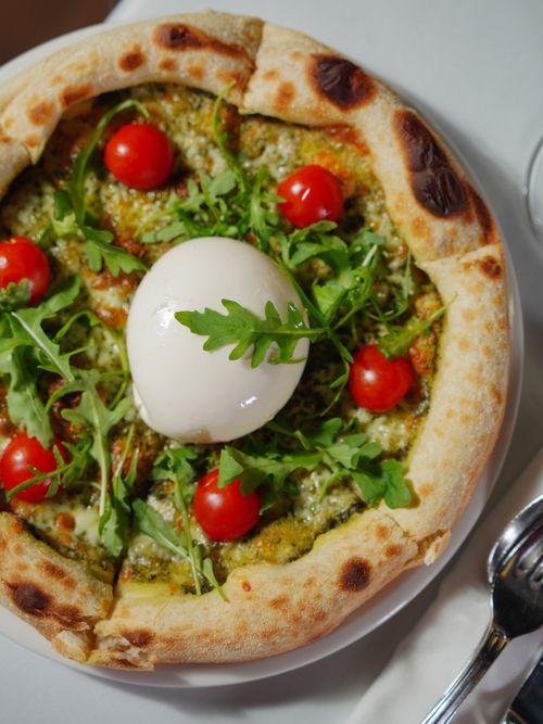 Free Close-up of a fresh pesto pizza topped with burrata cheese, cherry tomatoes, and arugula leaves. Stock Photo