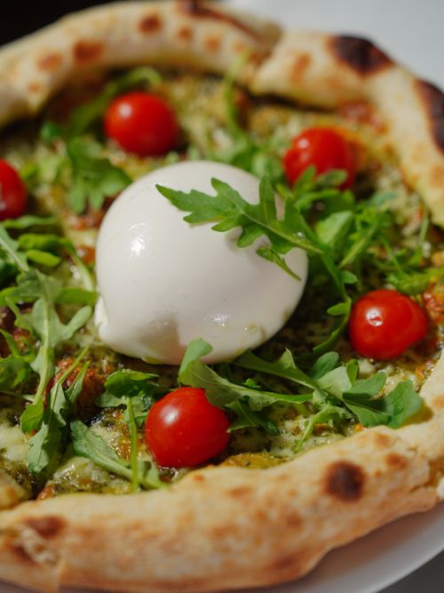 Free Tantalizing close-up of Italian pizza topped with burrata, arugula, and cherry tomatoes. Stock Photo