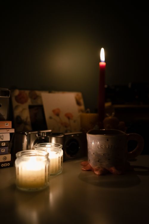 Free Warm candlelit ambiance with books, a mug, and camera creating a cozy evening scene. Stock Photo