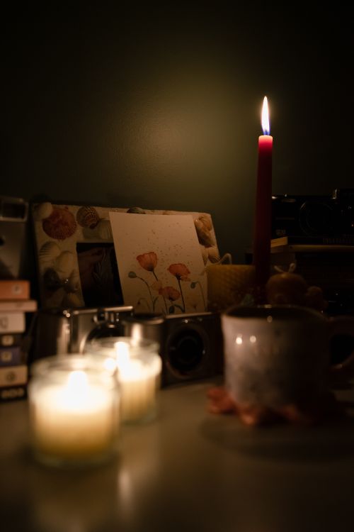 Free A warm candlelit desk setup with books, art, and a mug for a cozy, creative atmosphere. Stock Photo
