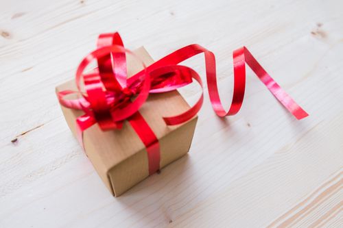 Free Elegant gift box with red ribbon on a light wooden background, ideal for celebrations. Stock Photo