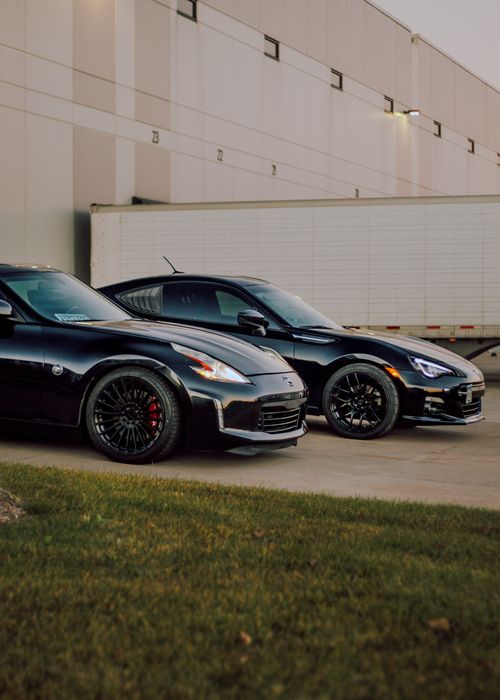 Free Two black sports cars parked outside an industrial warehouse, showcasing automotive elegance. Stock Photo